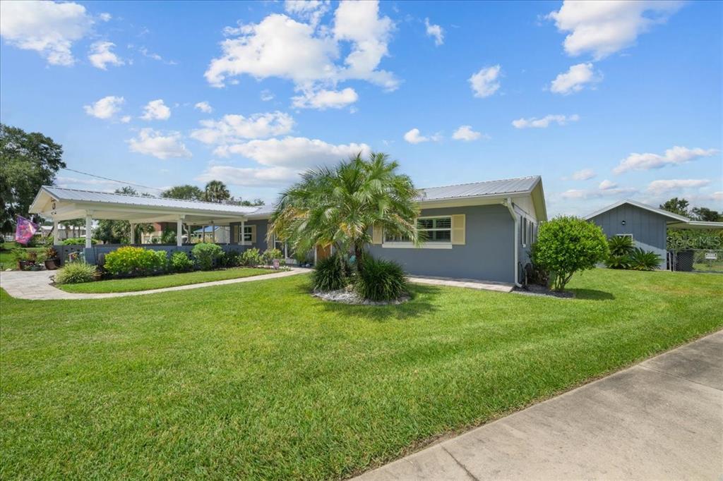 A gray single-story house features a metal roof, a covered carport, and a grassy lawn — 209 RIVER DRIVE, EAST PALATKA, FL
