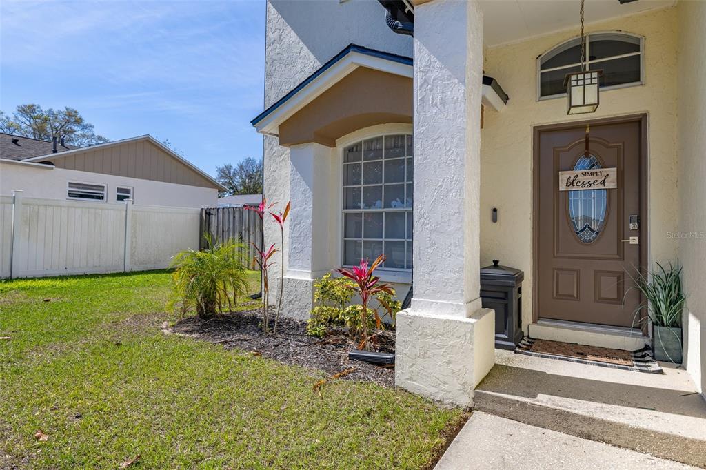 A brown front door with a decorative sign sits under a covered entryway with landscaping — 2313 DUNCAN TRAIL, CLERMONT, FL