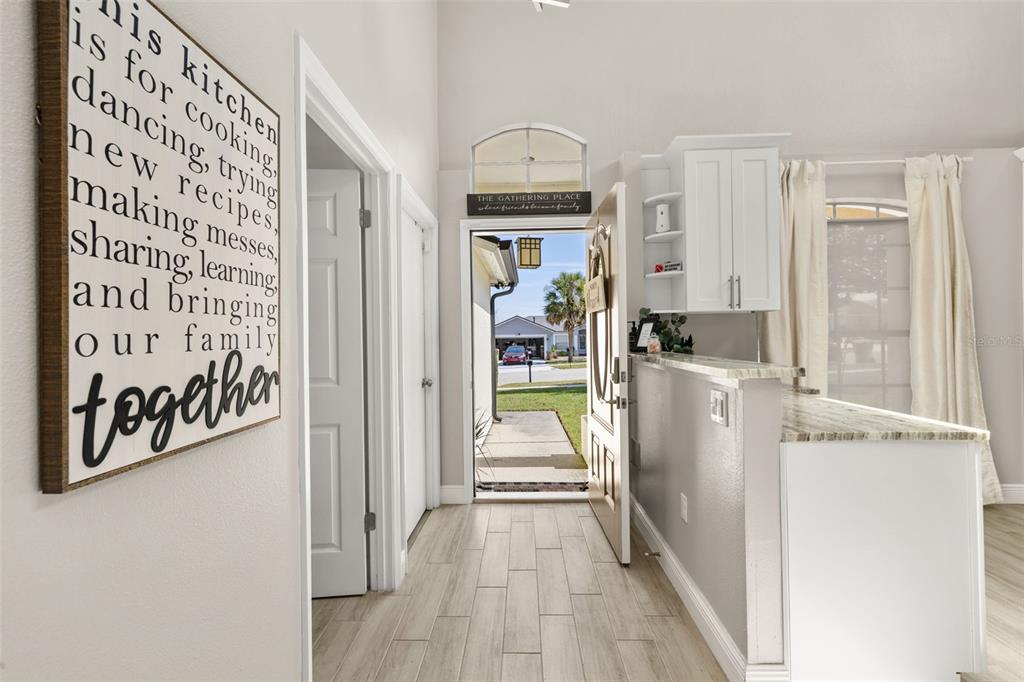 A kitchen entrance features light wood-look tile flooring, white cabinetry, and a large wall sign — 2313 DUNCAN TRAIL, CLERMONT, FL
