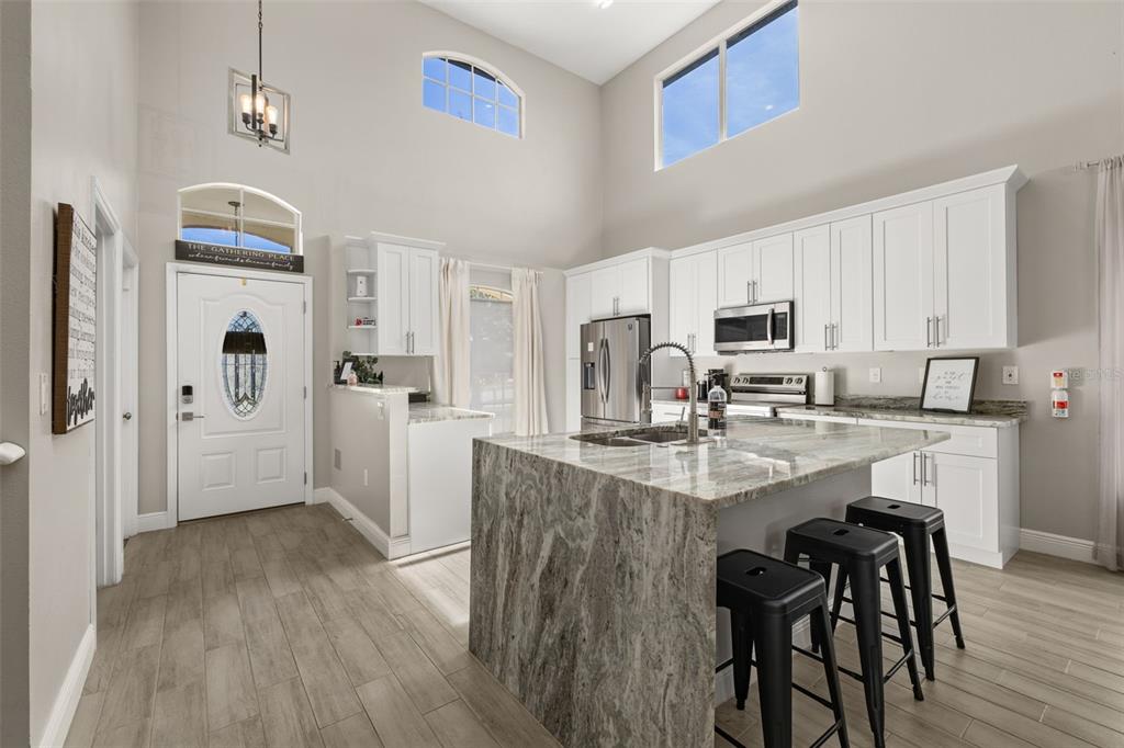 A kitchen with white cabinets, a large granite island, and high ceilings with tall windows — 2313 DUNCAN TRAIL, CLERMONT, FL