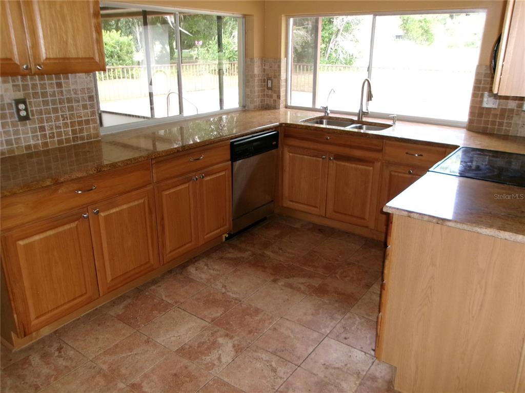 A kitchen features wood cabinets, granite countertops, tile flooring, and a double sink — 12709 CLOCK TOWER PARKWAY, HUDSON, FL