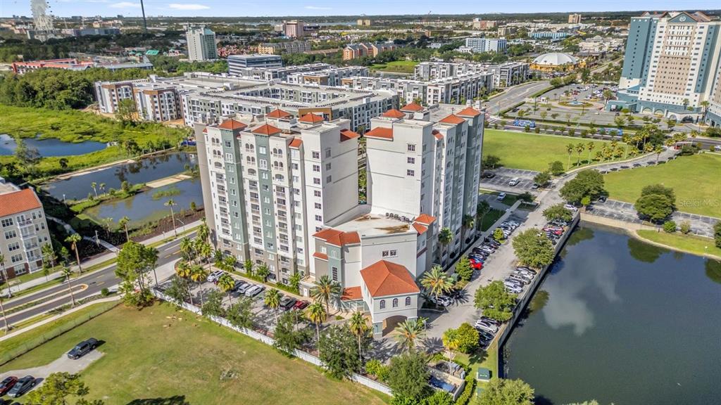 An aerial view shows a multi-story apartment building with a red tile roof near water — 7395 UNIVERSAL BLVD UNIT 402, ORLANDO, FL