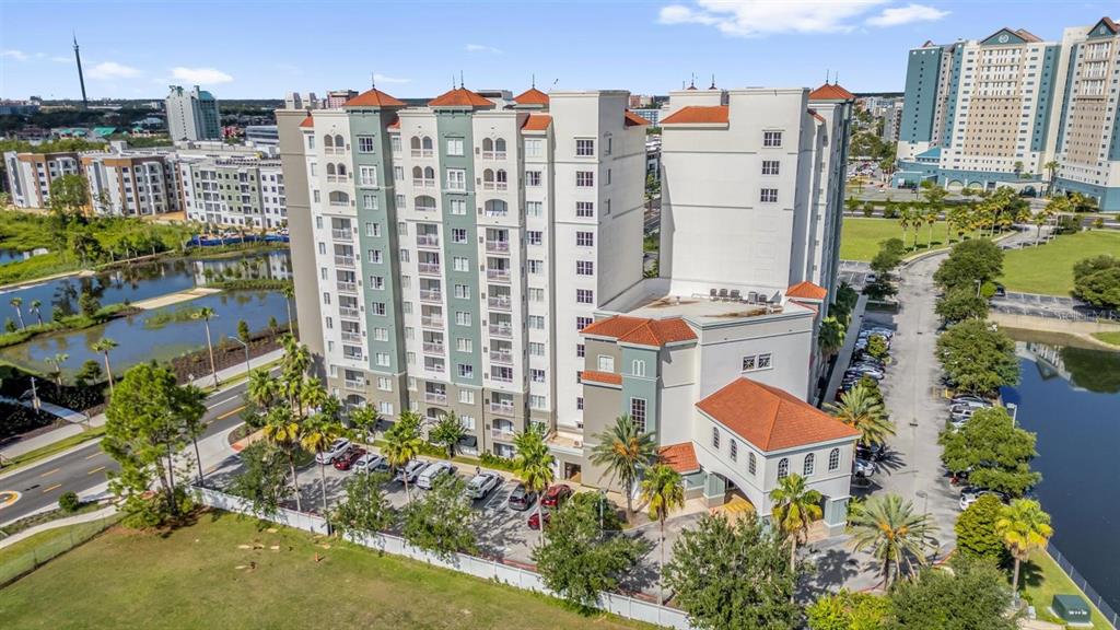 An aerial view shows a multi-story apartment building with a parking lot and pond — 7395 UNIVERSAL BLVD UNIT 402, ORLANDO, FL