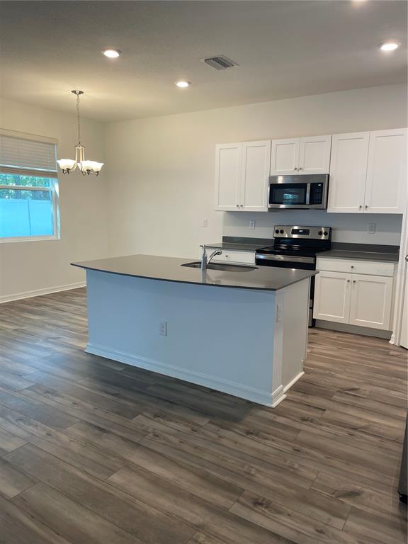 A kitchen features white cabinets, a central island with a sink, and wood-look flooring — 34772 MULRION DRIVE, ZEPHYRHILLS, FL