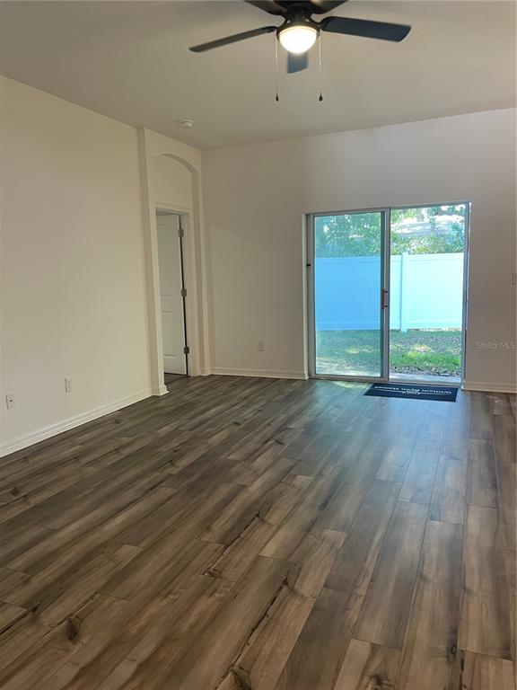 An empty room features wood-look flooring, a ceiling fan, and sliding glass doors to a yard — 34772 MULRION DRIVE, ZEPHYRHILLS, FL