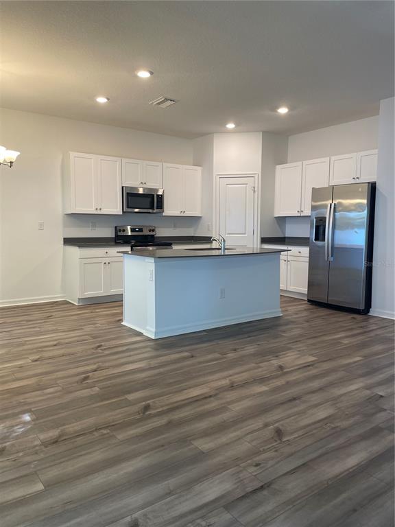 A kitchen with white cabinets, stainless steel appliances, a center island, and wood-look flooring — 34772 MULRION DRIVE, ZEPHYRHILLS, FL