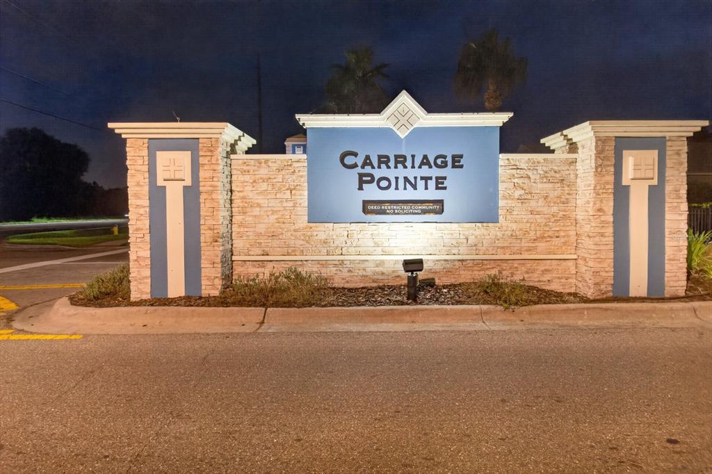 A stone-clad monument sign for the Carriage Pointe community stands at an entrance at night — 7961 CARRIAGE POINTE DRIVE, GIBSONTON, FL