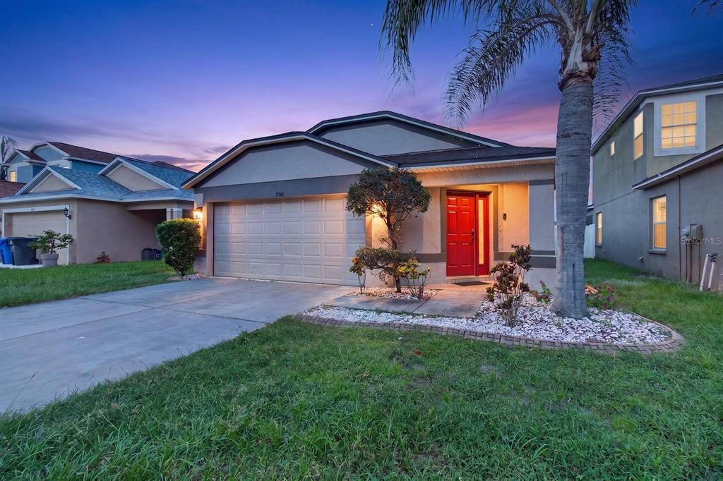 A single-story suburban house with a red front door, two-car garage, and a palm tree — 7961 CARRIAGE POINTE DRIVE, GIBSONTON, FL