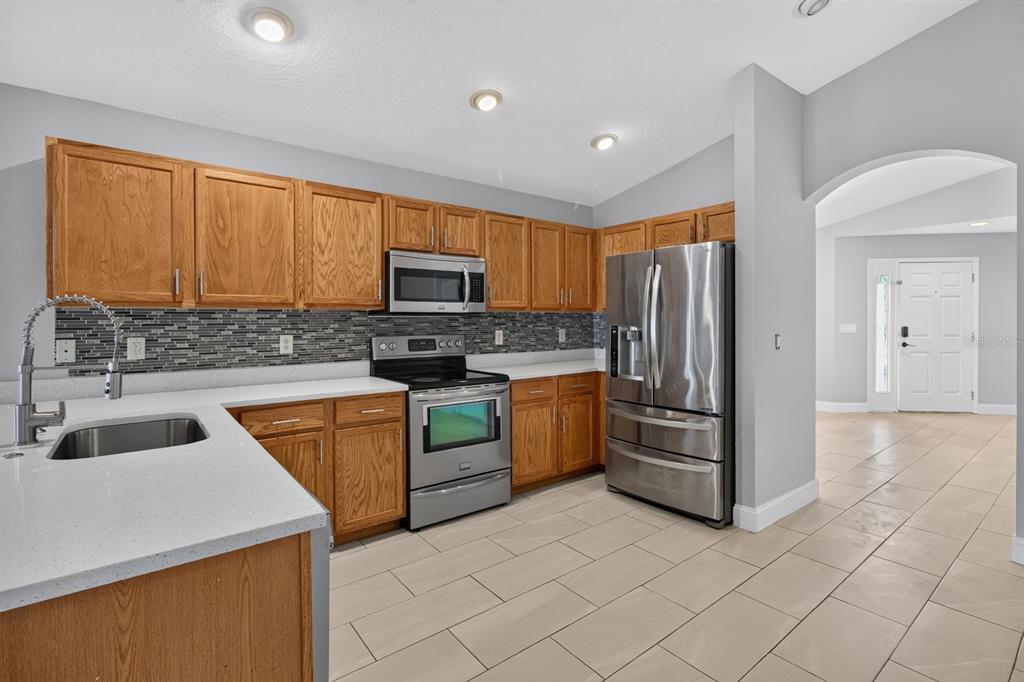 A kitchen with oak cabinets, stainless steel appliances, a tiled backsplash, and light-colored countertops — 7961 CARRIAGE POINTE DRIVE, GIBSONTON, FL
