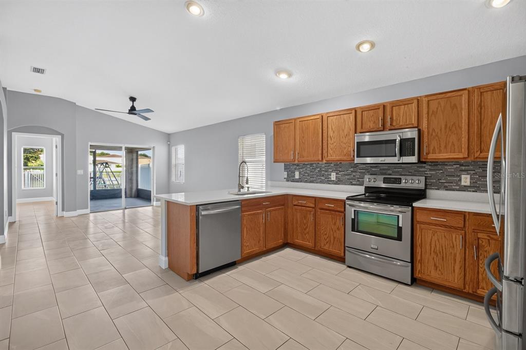 A kitchen with wood cabinets, stainless steel appliances, and tile flooring opens to a patio — 7961 CARRIAGE POINTE DRIVE, GIBSONTON, FL