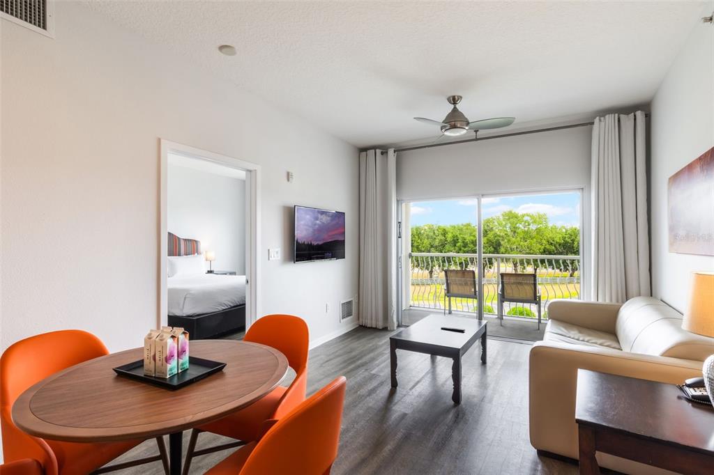 A living room and dining area with orange chairs, a sofa, and a balcony view — 225 CELEBRATION PLACE UNIT 401, KISSIMMEE, FL