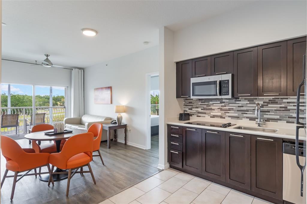 A kitchen with dark cabinets and a dining area with orange chairs overlook a balcony — 225 CELEBRATION PLACE UNIT 401, KISSIMMEE, FL