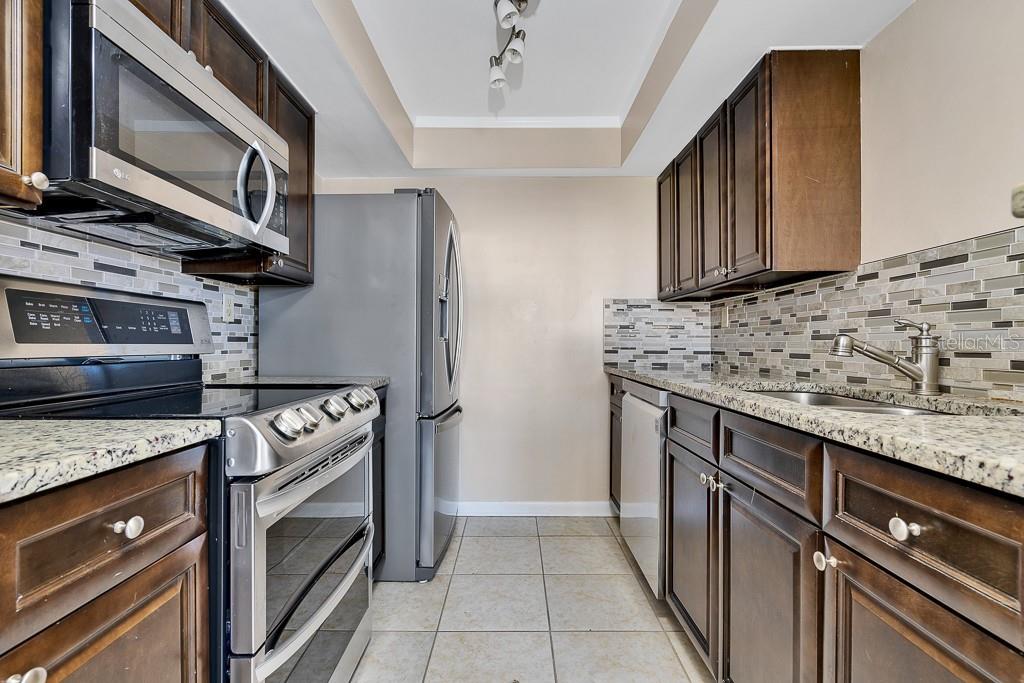 A galley kitchen features dark wood cabinets, stainless steel appliances, granite countertops, and a tiled backsplash — 223 DOLPHIN POINT, CLEARWATER BEACH, FL
