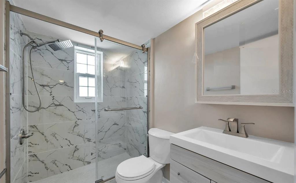 A bathroom features a marble-tiled walk-in shower, a white vanity, and a toilet — 223 DOLPHIN POINT, CLEARWATER BEACH, FL