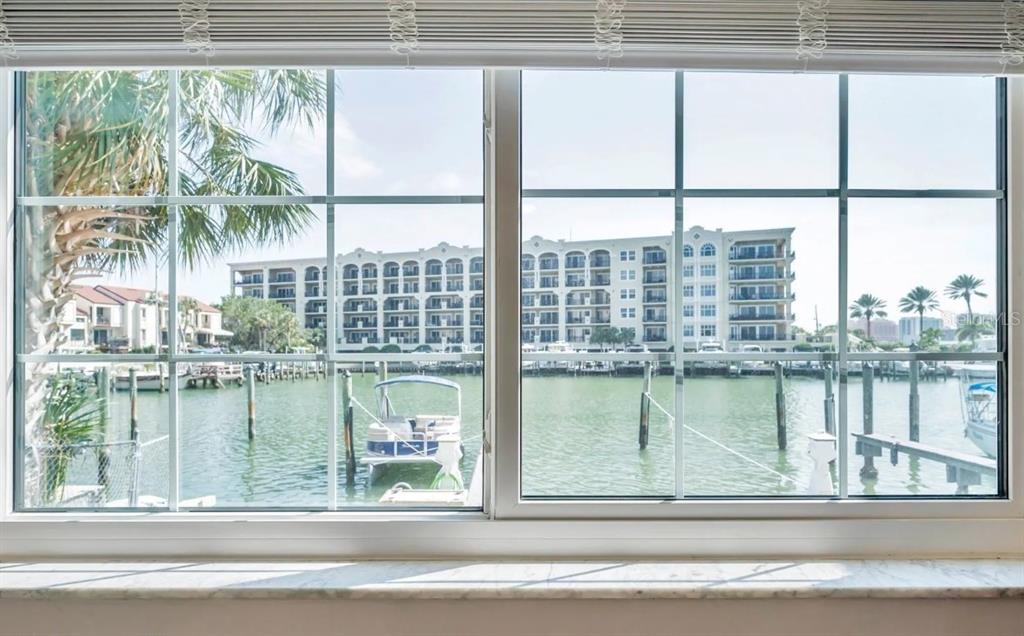 A view through a window overlooking a marina with boats and a large apartment building — 223 DOLPHIN POINT, CLEARWATER BEACH, FL