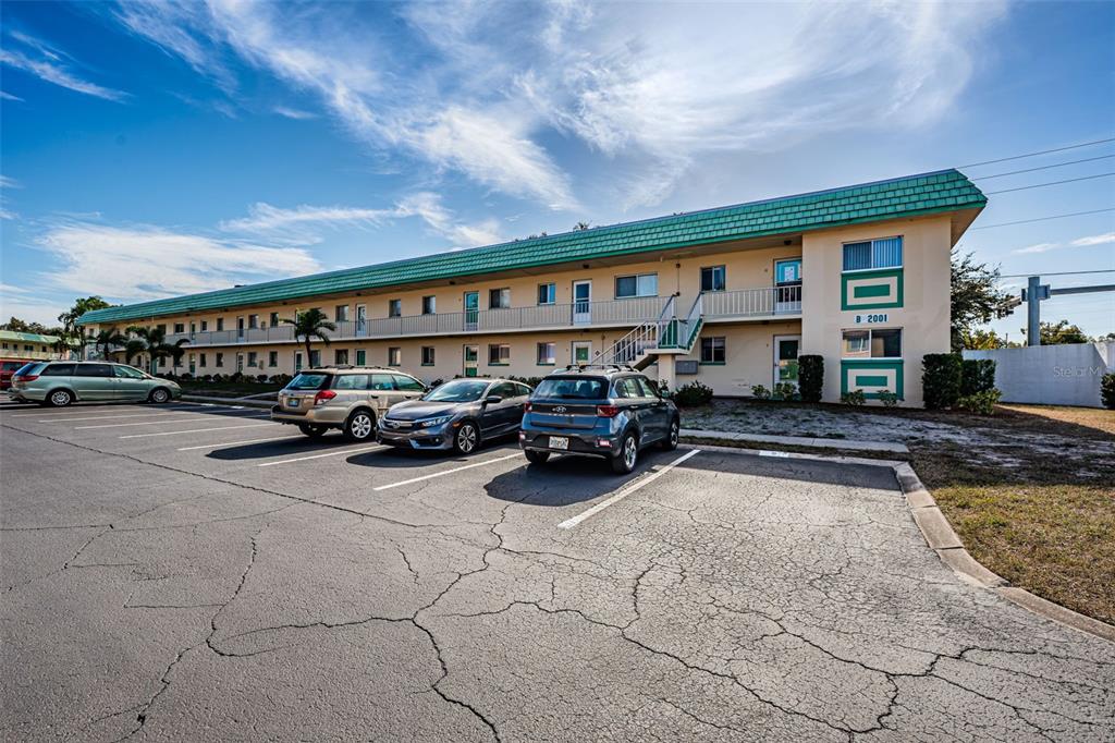 A two-story apartment building with a green roof and parking lot in the foreground — 2001 GREENBRIAR BOULEVARD UNIT 6, CLEARWATER, FL