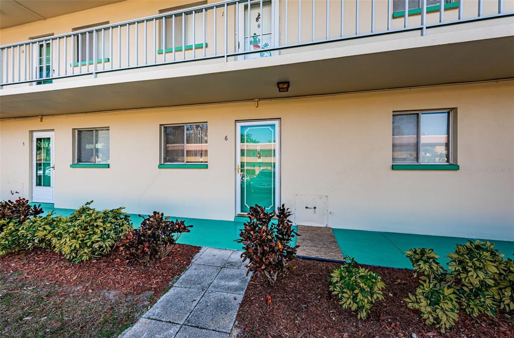 The exterior of a two-story apartment building features a walkway, numbered doors, and landscaping — 2001 GREENBRIAR BOULEVARD UNIT 6, CLEARWATER, FL