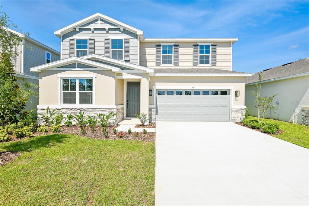 A two-story suburban house with beige siding, a stone facade, and a two-car garage — 141 WATERSTONE LOOP, TAVARES, FL