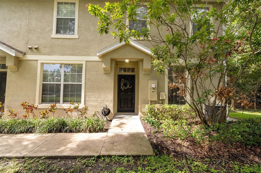 A two-story tan townhouse exterior features a black front door with a "hi" sign — 6717 EAGLE FEATHER DRIVE, RIVERVIEW, FL
