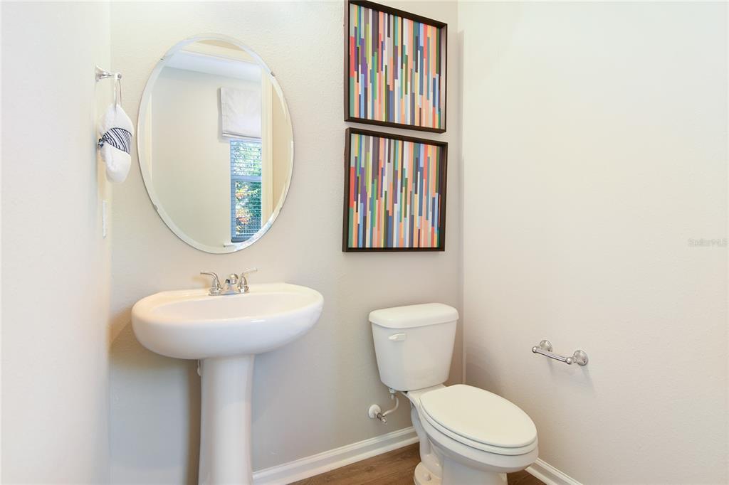 A bathroom with a pedestal sink, oval mirror, toilet, and two colorful abstract wall art pieces — 761 LAKE DELL AVENUE, DUNDEE, FL