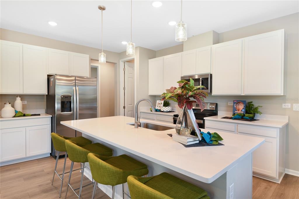 A modern kitchen features white cabinetry, a large central island with green stools, and stainless appliances — 761 LAKE DELL AVENUE, DUNDEE, FL