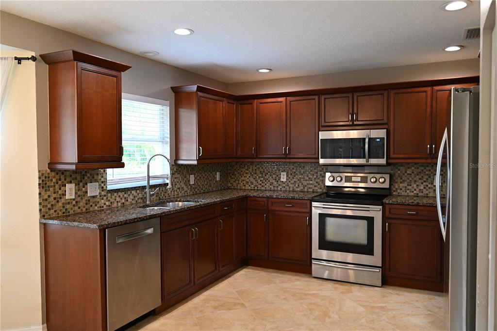 A kitchen with dark wood cabinets, granite countertops, stainless steel appliances, and a mosaic backsplash — 2043 OLD TRENTON LANE, SARASOTA, FL