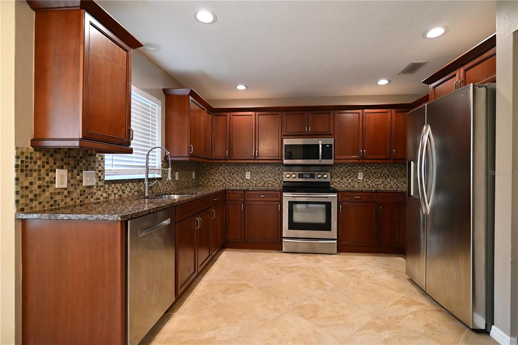 A kitchen features dark wood cabinets, stainless steel appliances, granite countertops, and a tiled backsplash — 2043 OLD TRENTON LANE, SARASOTA, FL