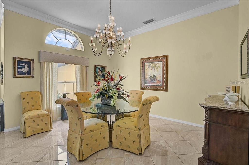 A dining room features a glass table, yellow patterned chairs, a chandelier, and tile flooring — 5072 KILTY COURT E, BRADENTON, FL