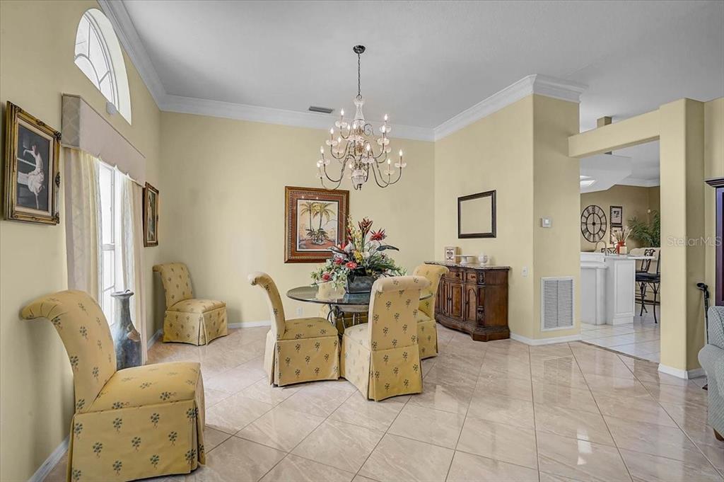 A dining room with yellow walls, tile floors, a glass table, and a crystal chandelier — 5072 KILTY COURT E, BRADENTON, FL