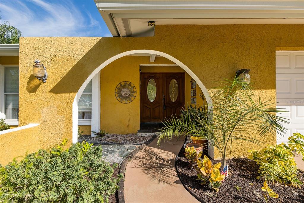 The exterior of a yellow house features a curved archway leading to a wooden double door — 11555 PINE STREET, SEMINOLE, FL