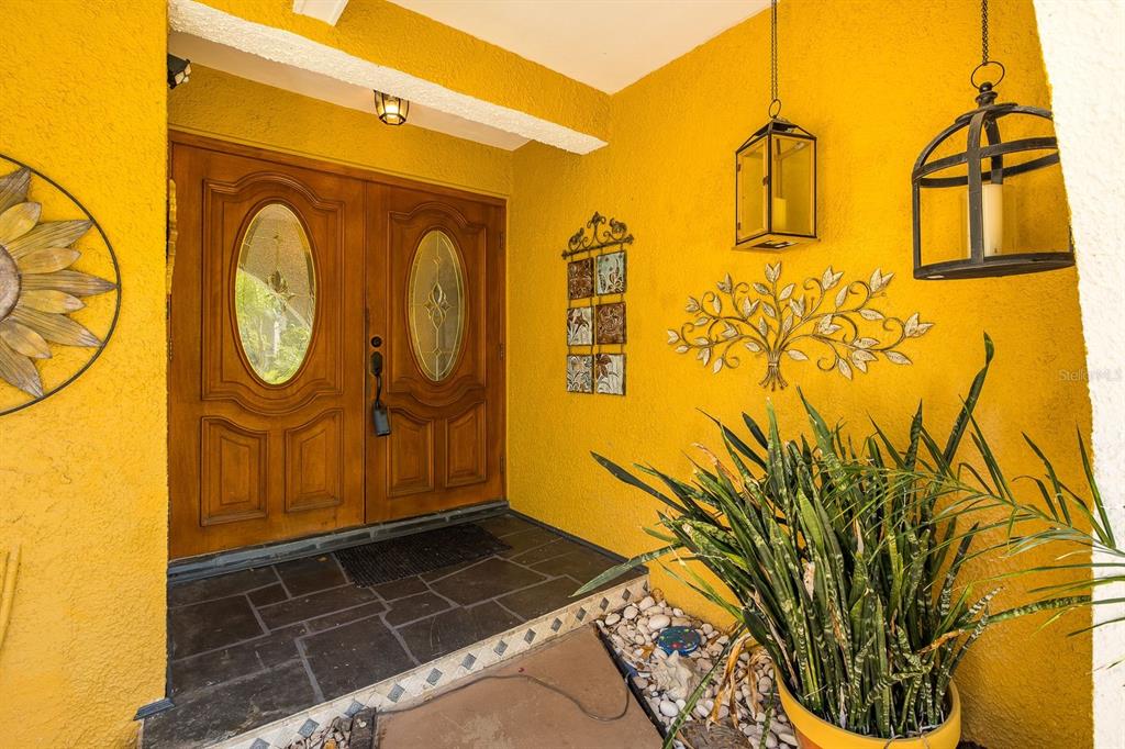 A bright yellow entryway features double wooden doors, stone flooring, and decorative wall art — 11555 PINE STREET, SEMINOLE, FL