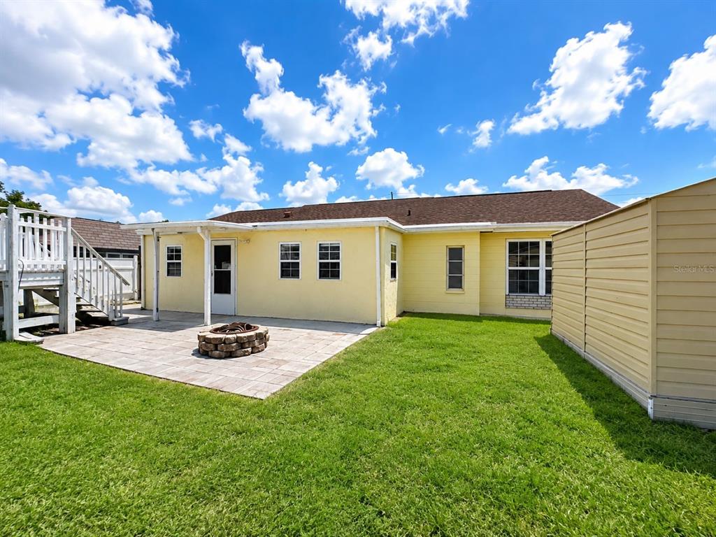The exterior of a yellow house features a stone fire pit on a paved patio — 3153 MOOG ROAD, HOLIDAY, FL