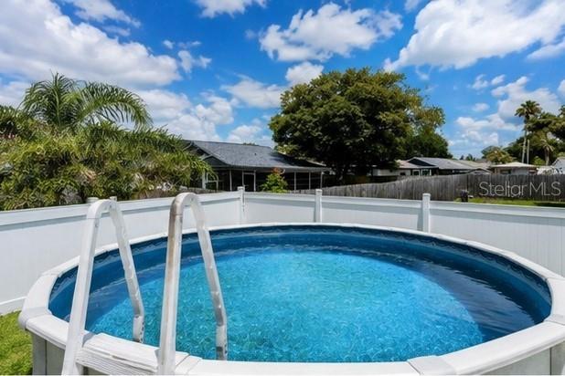 A round above-ground swimming pool sits in a backyard enclosed by a white vinyl fence — 3153 MOOG ROAD, HOLIDAY, FL