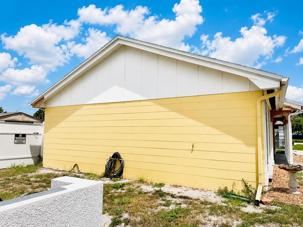 The exterior side of a yellow house features horizontal siding, a white gable, and a downspout — 3153 MOOG ROAD, HOLIDAY, FL