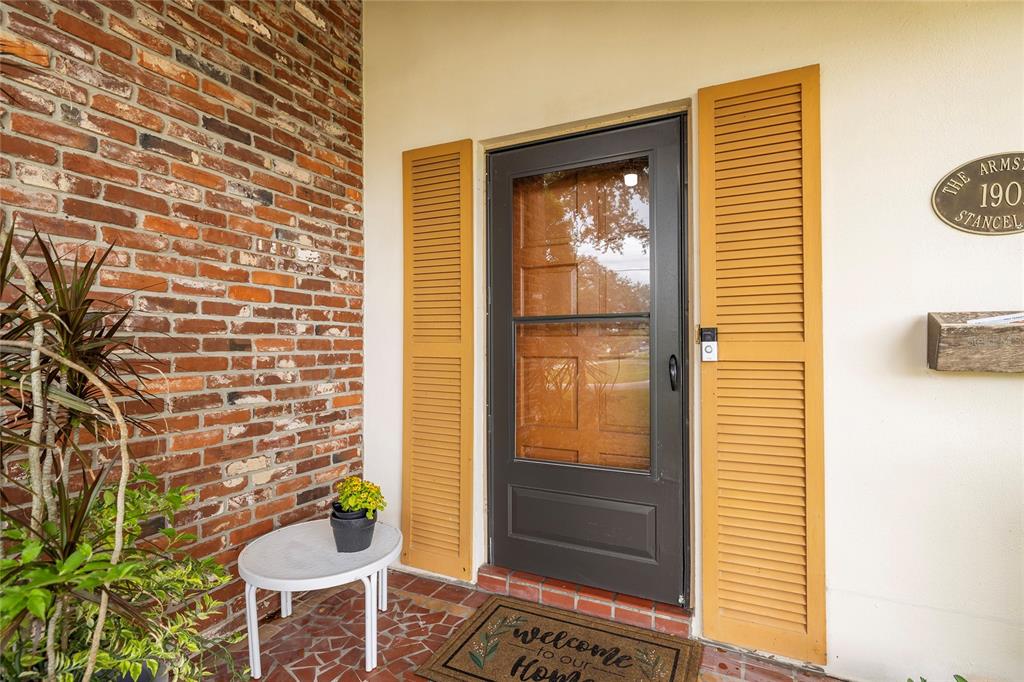 A front entryway features a brick wall, a dark storm door, and yellow shutters — 1901 STANCEL DRIVE, CLEARWATER, FL
