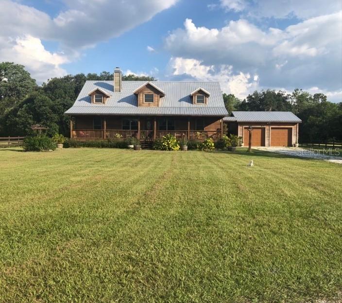 A two-story log cabin home with a metal roof and detached garage sits on grass — 2405 N RYE ROAD, PARRISH, FL