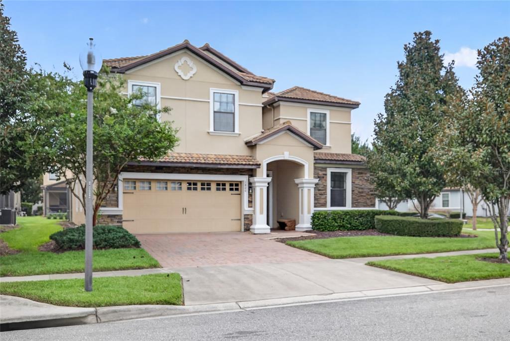 A two-story suburban house with a tan stucco exterior, stone accents, and a two-car garage — 1400 WEXFORD WAY, DAVENPORT, FL