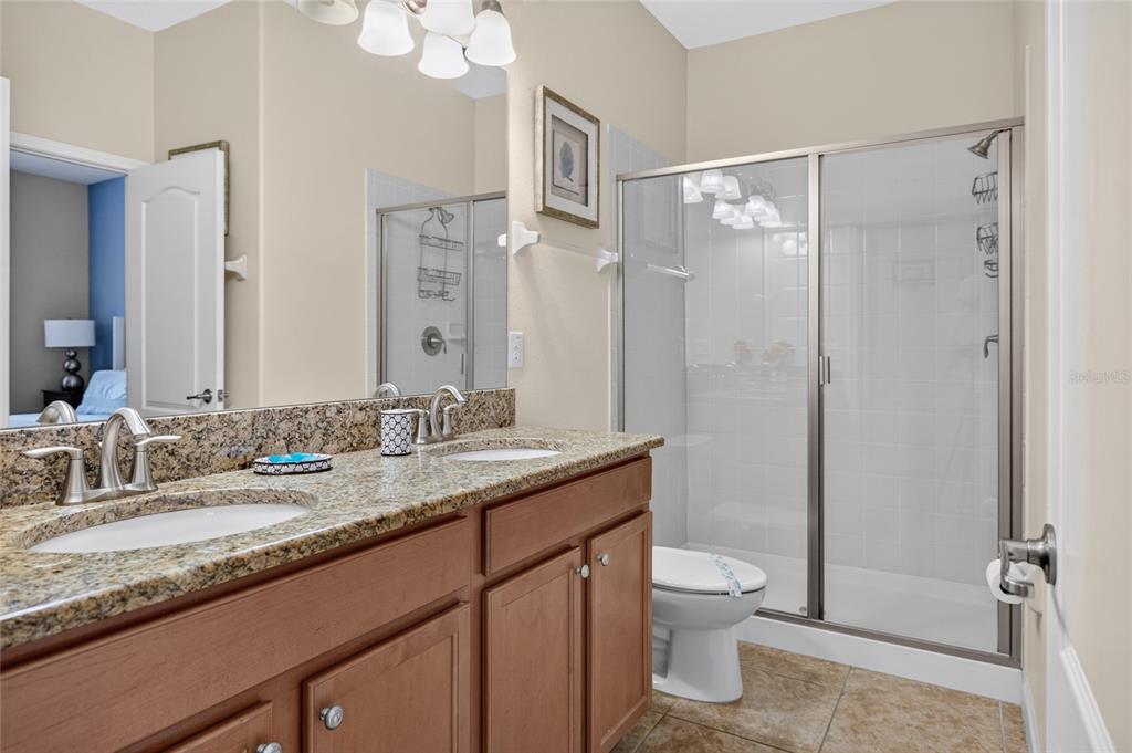 A bathroom features a double vanity with granite countertops, wood cabinets, and a glass shower — 1400 WEXFORD WAY, DAVENPORT, FL