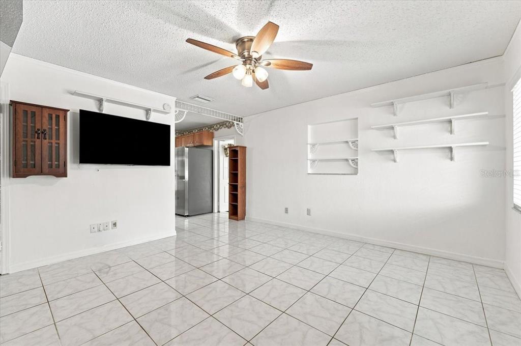 A living room with white tile floors, a ceiling fan, and a wall-mounted television — 122 W COLLINS STREET, LAKELAND, FL
