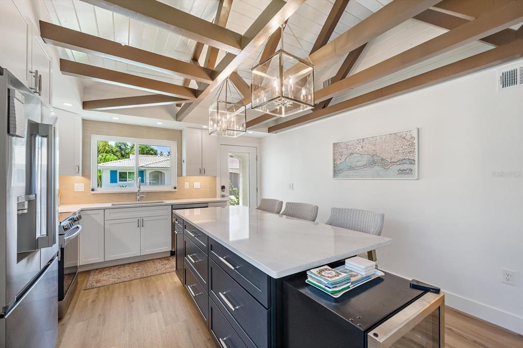 A kitchen features a dark island with a white countertop, wooden ceiling beams, and cabinetry — 711 SPANISH DRIVE S UNIT 211, LONGBOAT KEY, FL