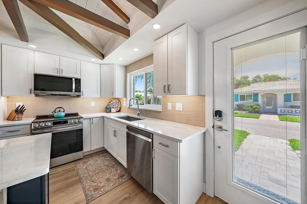A modern kitchen features white cabinetry, stainless steel appliances, and a vaulted ceiling with beams — 711 SPANISH DRIVE S UNIT 211, LONGBOAT KEY, FL