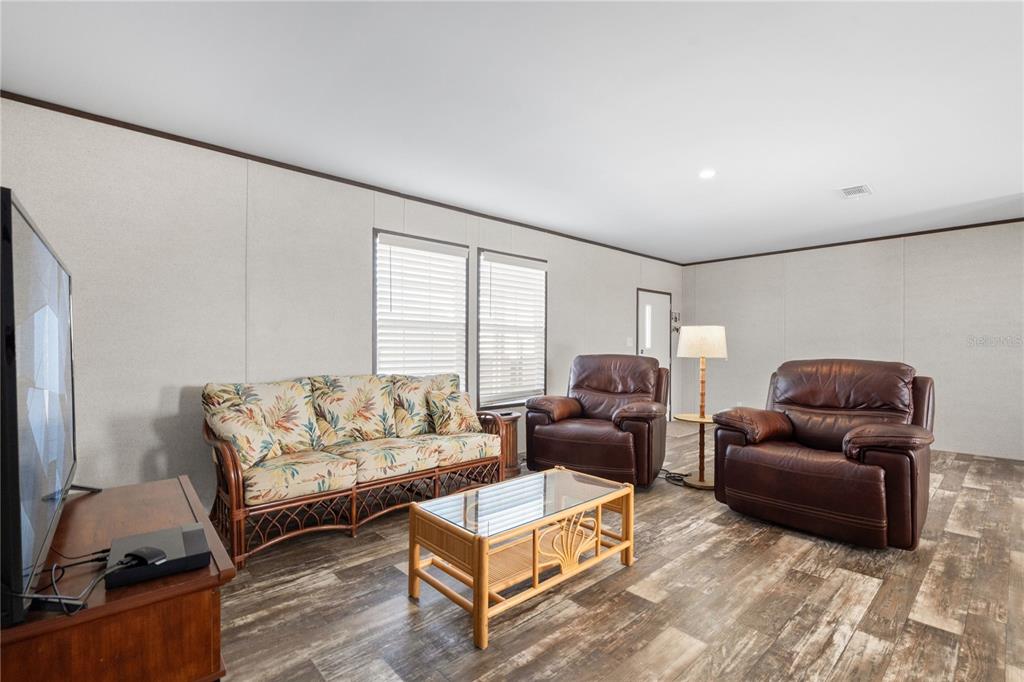 A living room features a floral sofa, two leather recliners, a glass coffee table, and wood-look flooring — 224 WOLVERINE AVENUE, NORTH PORT, FL