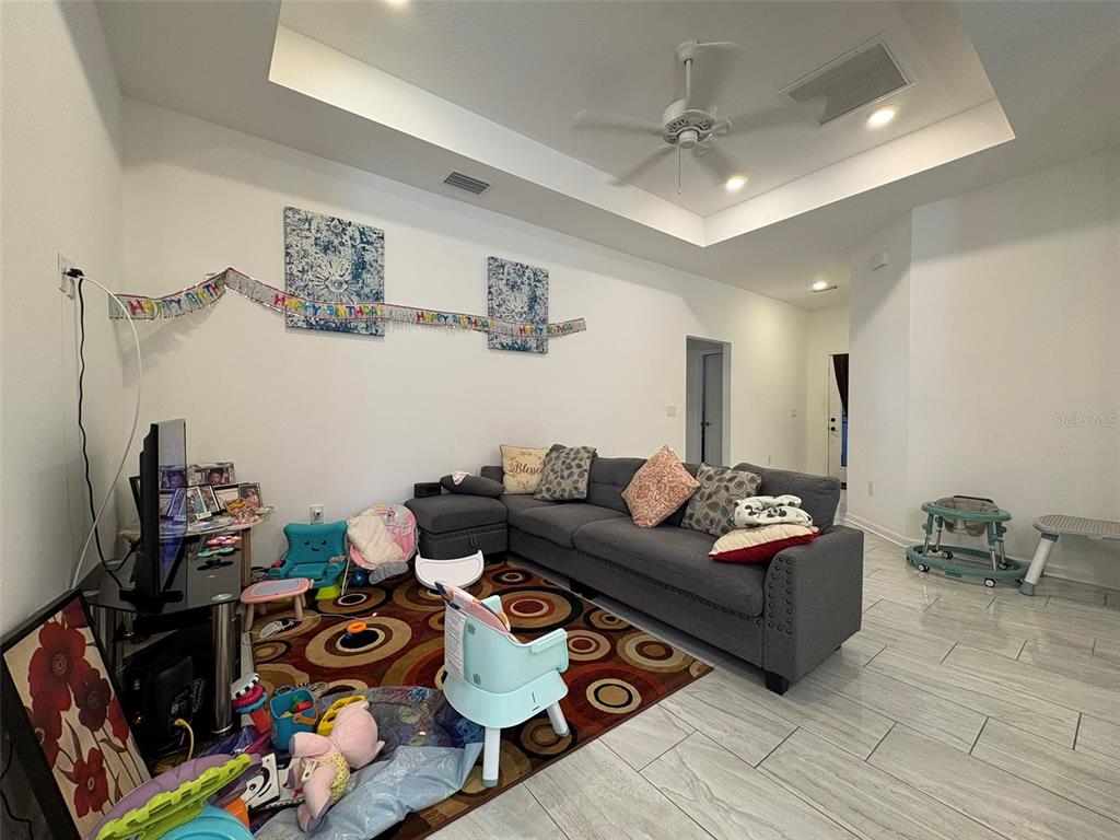 A living room with a gray sectional sofa, a patterned rug, and a tray ceiling — 22 DEACON JONES BOULEVARD, ORLANDO, FL