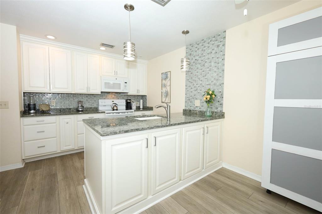 A kitchen features white cabinets, granite countertops, a tiled backsplash, and a central island — 2372 SUN VALLEY CIRCLE UNIT 2372, WINTER PARK, FL