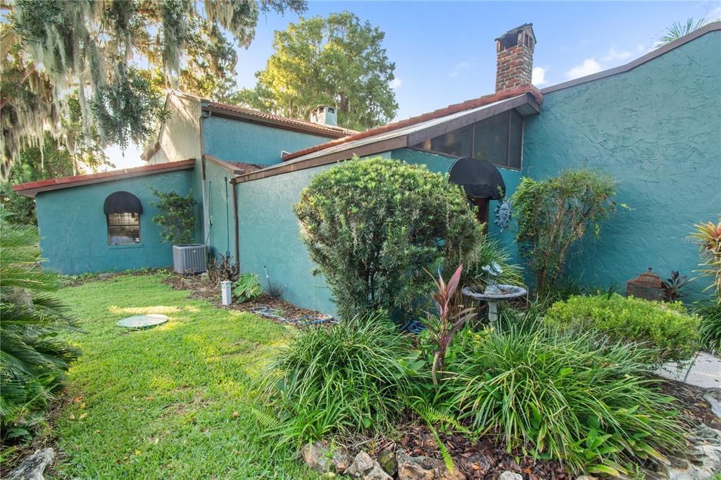 A concrete walkway leads to a teal-colored house entrance surrounded by lush landscaping and trees — 1019 W LAKE ELOISE TERRACE, WINTER HAVEN, FL