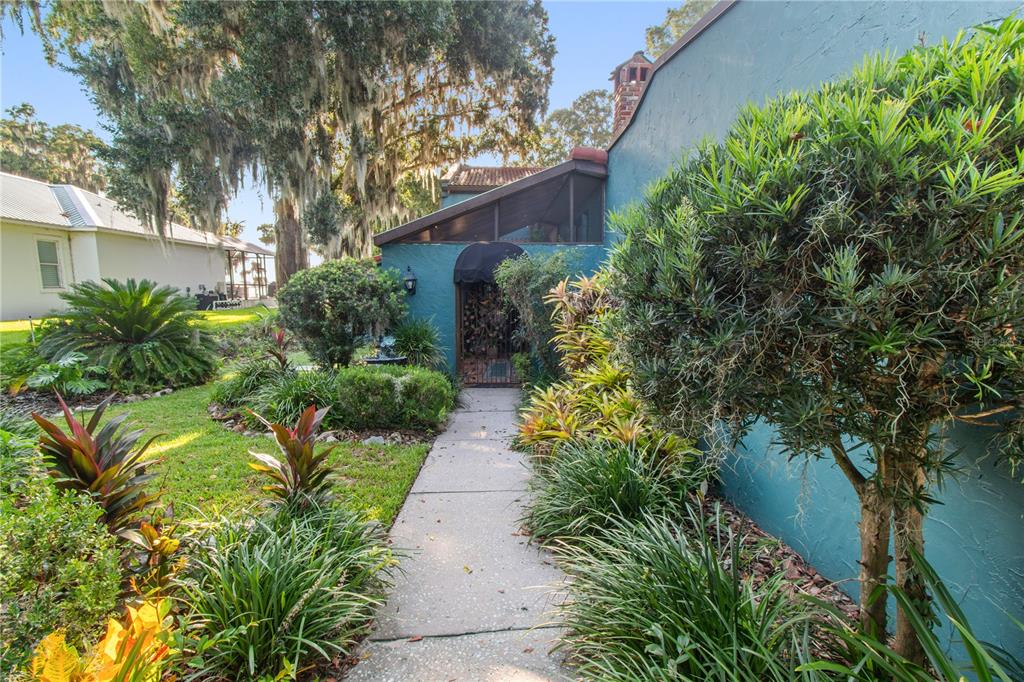 A teal stucco carport with arched openings sits beside a landscaped garden and walkway — 1019 W LAKE ELOISE TERRACE, WINTER HAVEN, FL