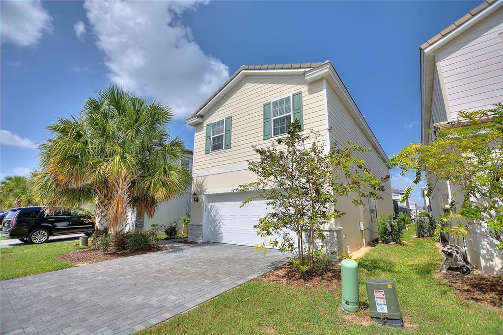A two-story house with beige siding, green shutters, a paved driveway, and a palm tree — 7384 OAKMOSS LOOP, DAVENPORT, FL