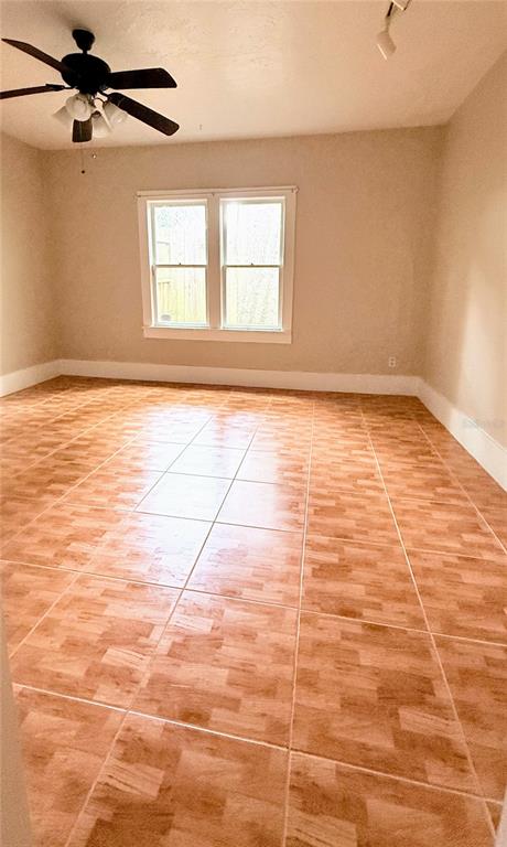 An empty room features light-colored walls, a ceiling fan, and brown square-tiled flooring — 808 NW 23RD AVENUE, GAINESVILLE, FL
