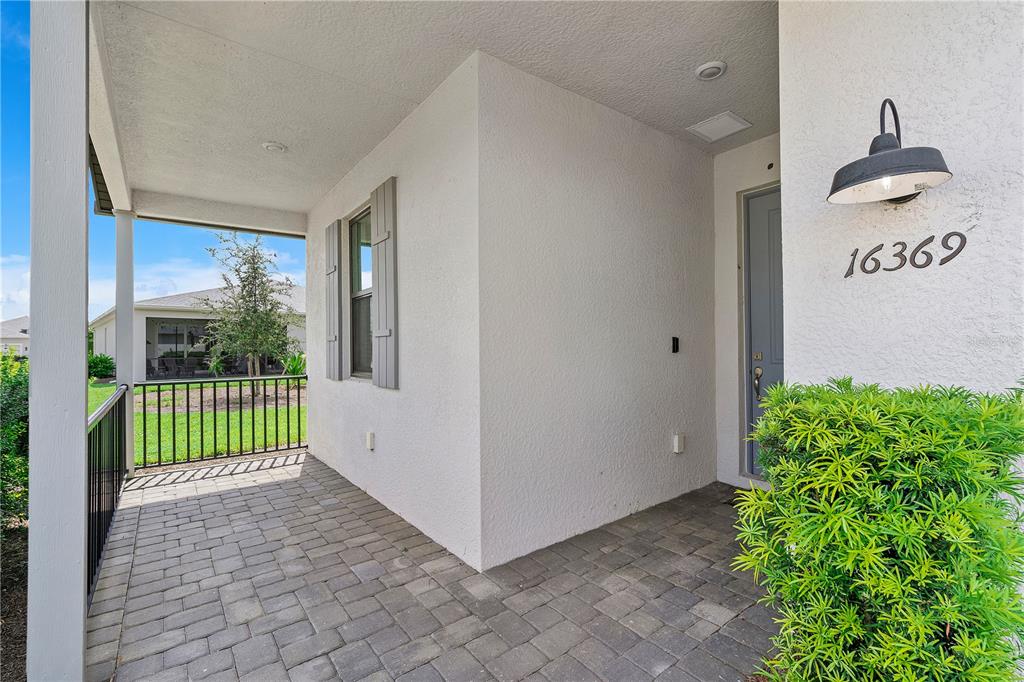 A covered front porch features gray paver flooring, a light-colored stucco wall, and a door — 16369 PALMETTO STREET, PUNTA GORDA, FL