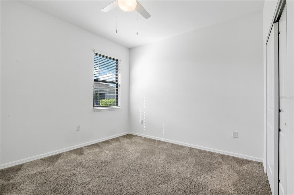 A small, empty bedroom with white walls, gray carpet, a ceiling fan, and a window — 16369 PALMETTO STREET, PUNTA GORDA, FL
